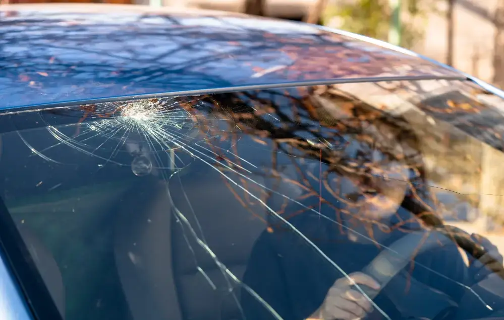 Geschockte Frau im Auto mit kaputter Windschutzscheibe und Rissen. 